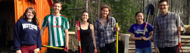 6 volunteers line up holding shovels standing in front of the brown compost shed in Northwoods Parking lot